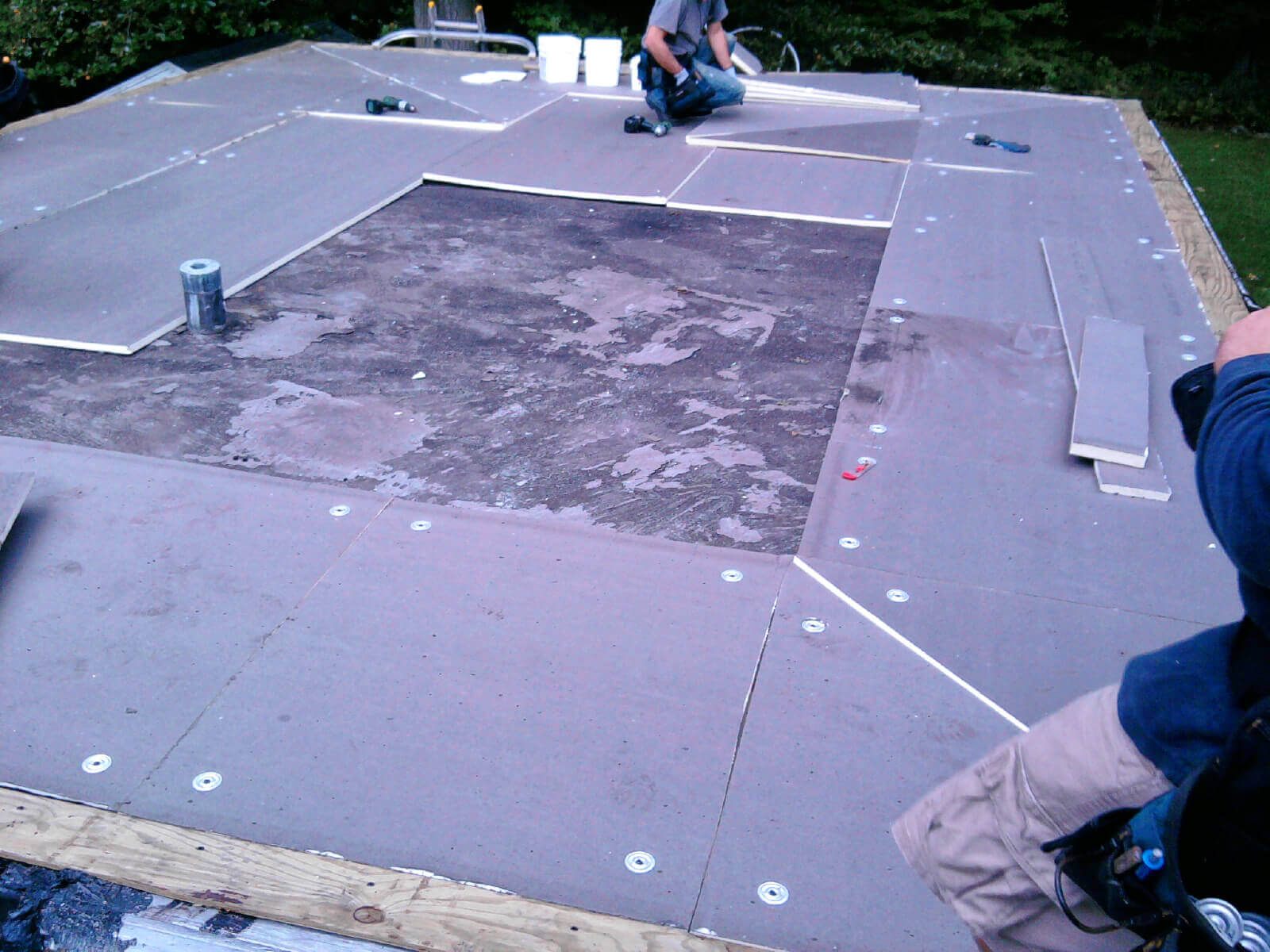Roofers fastening rigid insulation and cover boards over an old flat roof deck before a new membrane is installed