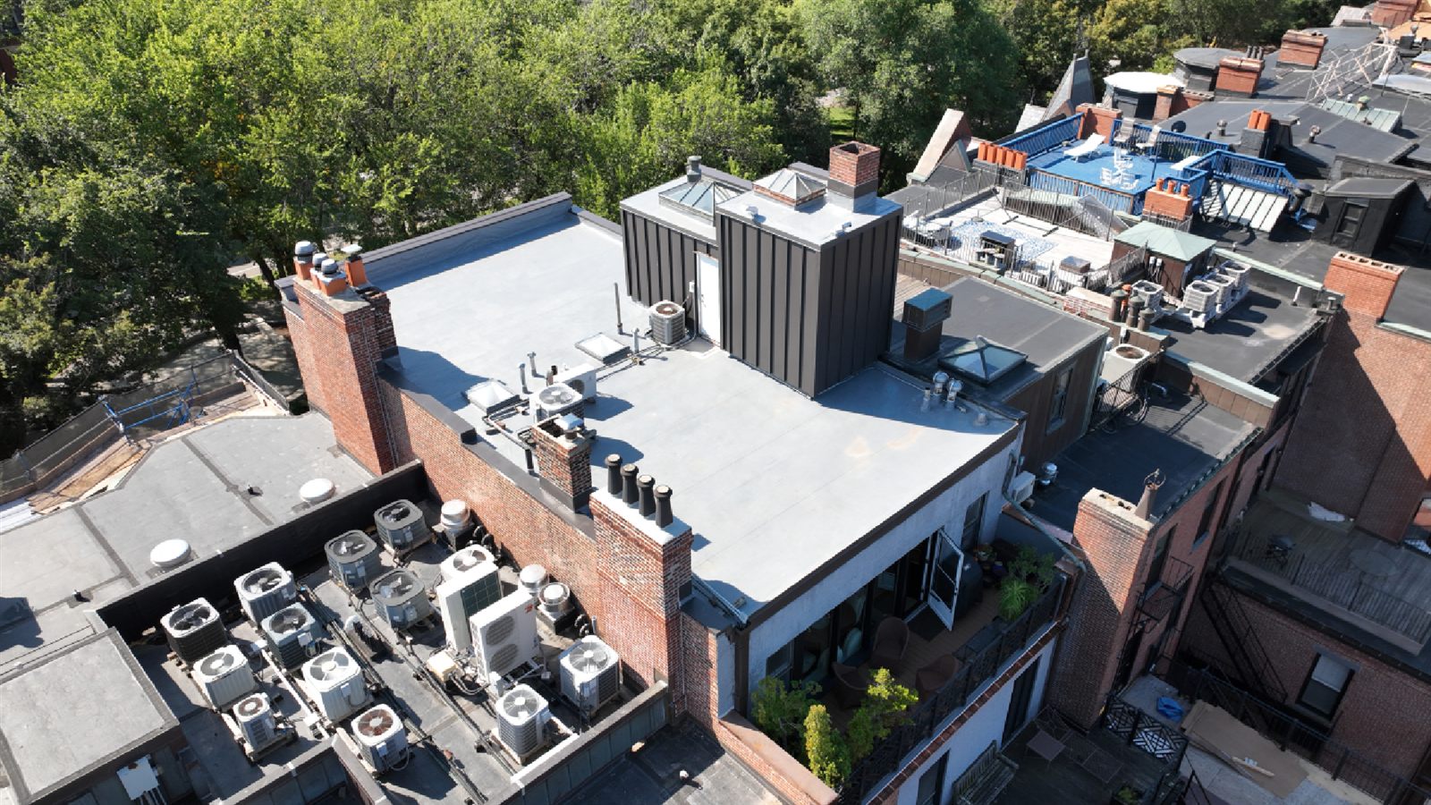 Drone view of a new gray PVC membrane roof on a brick Boston row house, with chimneys, skylights and rooftop HVAC units on the neighboring roofs