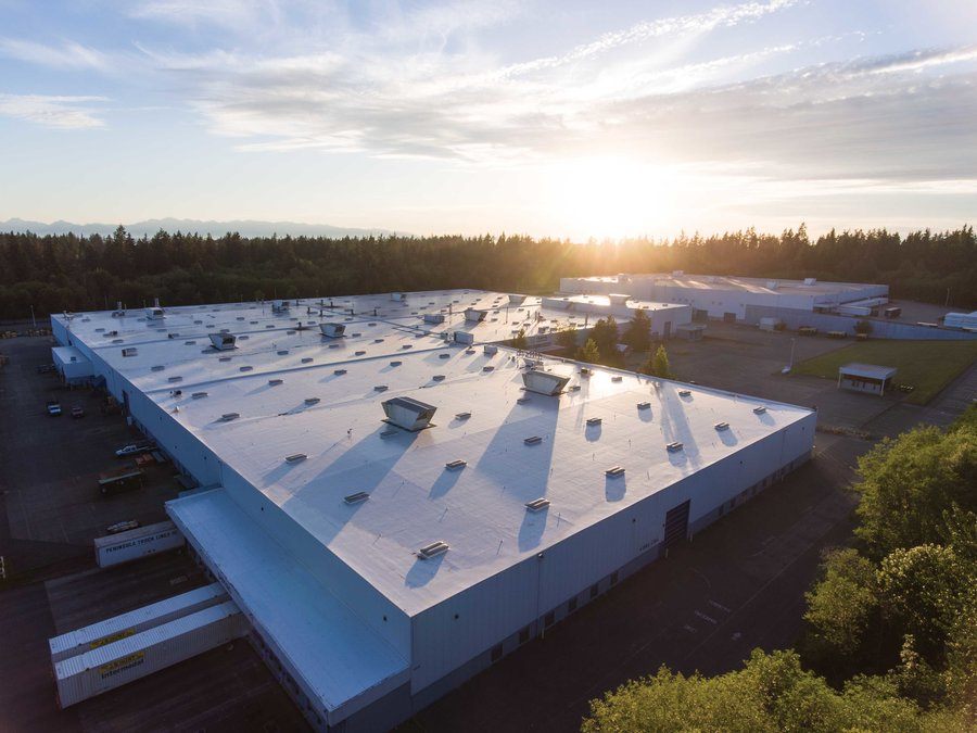 Aerial view at sunset of a large warehouse with a white single-ply membrane roof and rooftop vents